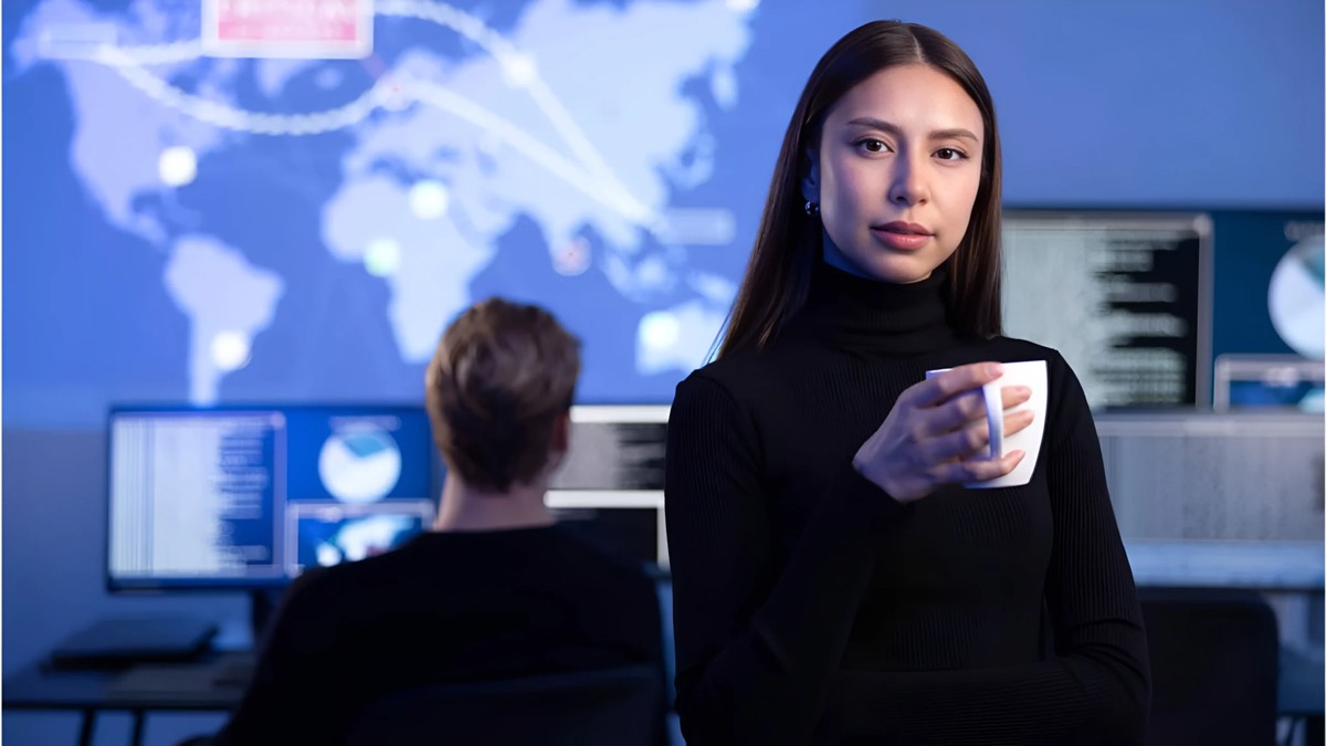 A security analyst standing in an operations room, with a global threat map behind her