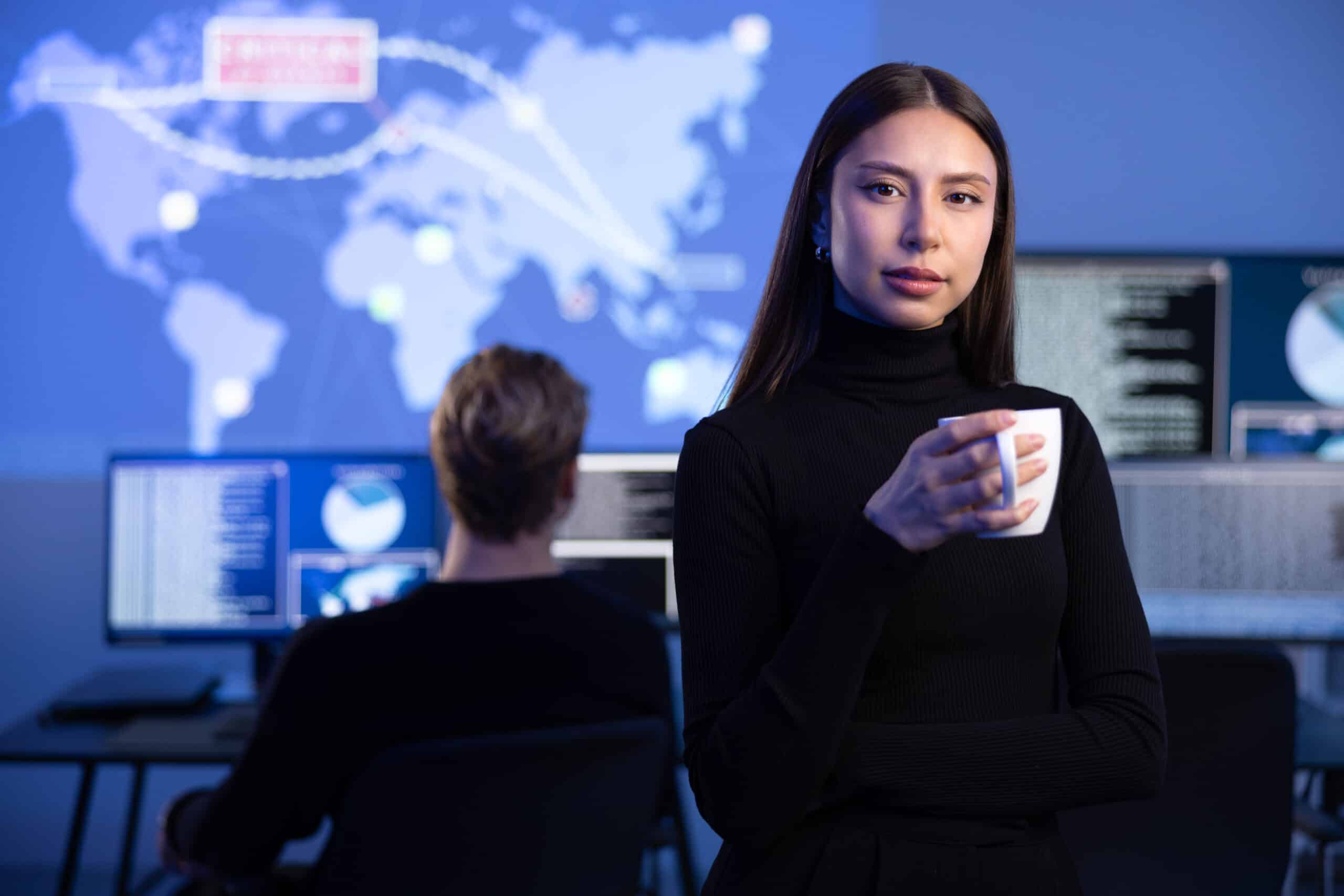 Professional Female IT Consultant holding coffee cup in large Cyber Security Operations Center SOC